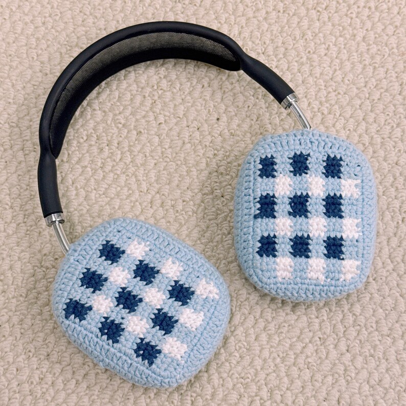 May include: Over-ear headphones with light blue and white checkered crochet ear covers. The headband is black with silver accents. The ear covers are a light blue color with a checkered pattern of white and dark blue squares.