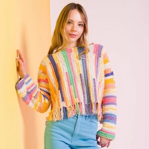 Könnte beinhalten: Ein langärmeliger Häkelpullover mit vertikalem Streifenmuster in verschiedenen Pastell- und leuchtenden Farben wie Gelb, Rosa, Grün, Blau und Weiß. Das Kleidungsstück hat einen verkürzten Saum mit langen, herabhängenden Fransen.