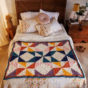 May include: A rectangular crochet blanket featuring a geometric pinwheel pattern. The design consists of triangular and square blocks in cream, mustard yellow, burnt orange, teal, navy blue, and lavender, finished with a dark teal border.