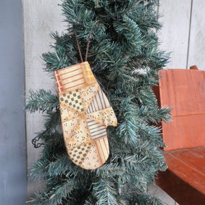 May include: A patchwork fabric mitten ornament in shades of yellow, brown, blue, and red hanging from a green artificial Christmas tree.