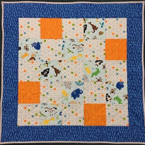May include: A blue and white baby quilt with a patchwork design featuring various animal illustrations. The quilt has a blue border with a geometric pattern.