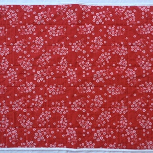 May include: Red fabric with a white floral pattern. The fabric is quilted and has a white border.
