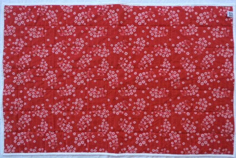 May include: Red fabric with a white floral pattern. The fabric is quilted and has a white border.
