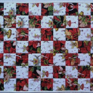 May include: A patchwork quilt with a checkerboard pattern featuring red poinsettia flowers and fairies with green wings. The quilt is made of white, red, green, and black fabric.