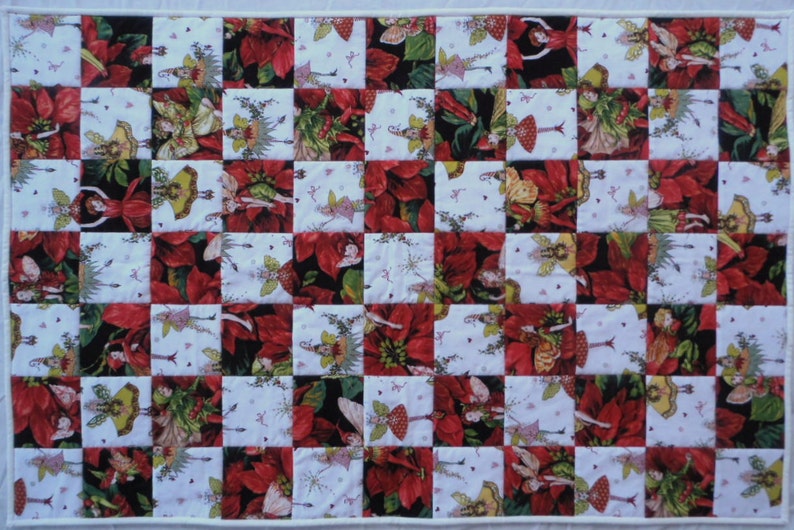 May include: A patchwork quilt with a checkerboard pattern featuring red poinsettia flowers and fairies with green wings. The quilt is made of white, red, green, and black fabric.