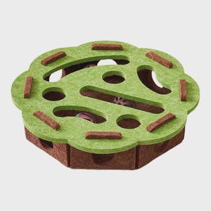 May include: A green and brown cat toy with a flower-shaped top. The toy has multiple holes and tunnels for play, with brown felt accents. The base is a darker brown, and the top is a lighter green.