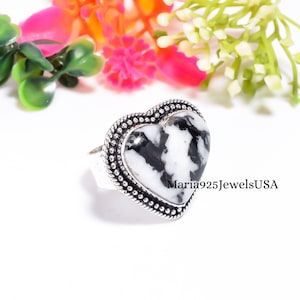 May include: A heart-shaped ring featuring a black and white patterned stone set in a silver band with a beaded border. The text Maria925JewelsUSA is visible on the right side of the ring. The design includes a polished stone surface.