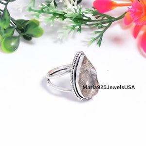 Peut inclure: Une bague en argent avec une pierre précieuse brute, translucide et brun clair en forme de poire, sertie dans un chaton en métal texturé. L'anneau se compose de deux fins fils d'argent polis qui se rejoignent sur les côtés. Texte Maria925JewelsUSA.