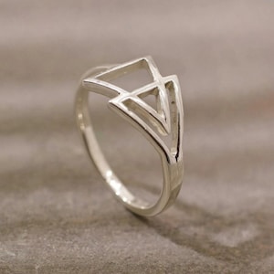Peut inclure: Une bague en argent avec un motif géométrique de triangles qui se chevauchent. La bague a une finition polie et est posée sur un fond neutre. Le design de la bague est moderne et minimaliste.