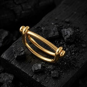 May include: A polished gold-tone metal ring featuring a unique double-band design that curves into a rounded, elongated shape. The piece has smooth, continuous lines and a reflective surface, showcasing a modern aesthetic with a sleek, metallic finish.