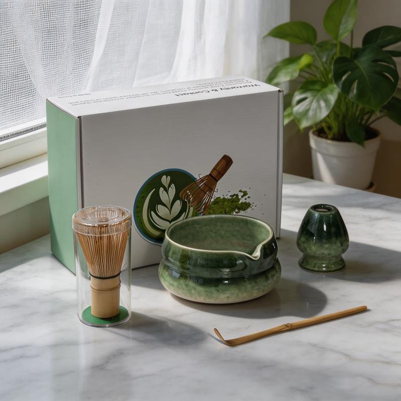 May include: A matcha tea set including a bamboo whisk in a clear cylindrical case, a green ceramic bowl with a pouring spout, a green ceramic whisk holder, and a bamboo scoop. The set is presented with a white box featuring a green logo.