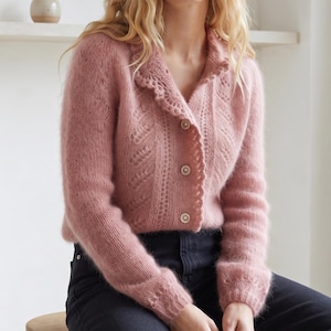 Può includere: Un cardigan rosa polvere a maniche lunghe con un delicato motivo a maglia traforata, un colletto smerlato e tre bottoni rotondi sul davanti. Il capo presenta una consistenza morbida e soffice ed è abbinato a jeans in denim grigio scuro.