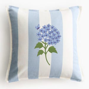 May include: Square throw pillow with a blue and white striped pattern. The pillow features a floral design of blue hydrangea flowers and a butterfly. The pillow has a white border.