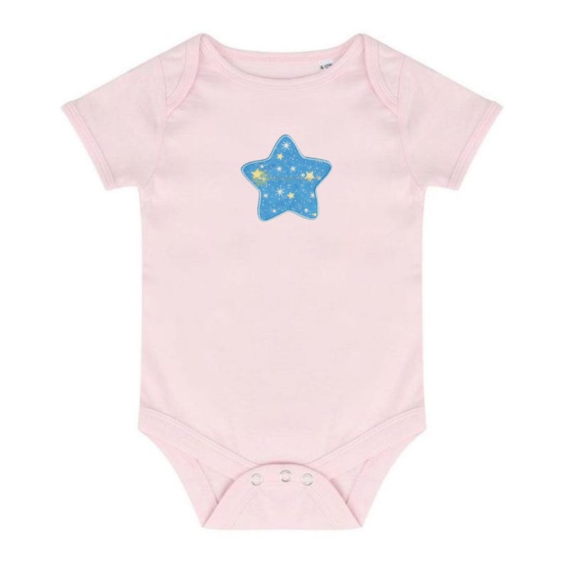 May include: A light pink baby onesie with short sleeves. The onesie features a blue star applique with a pattern of yellow stars. The onesie has snap closures at the bottom for easy diaper changes. The garment is made of soft material.