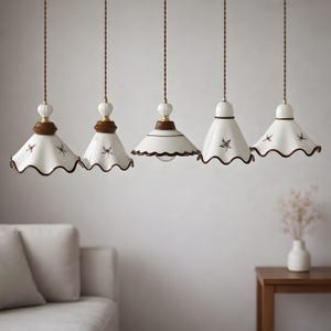 May include: Five pendant lights with white shades, brown scalloped edges, and decorative floral accents. The lights hang from brown cords, with a wooden and ceramic fixture at the top. The lights are suspended above a living room setting.
