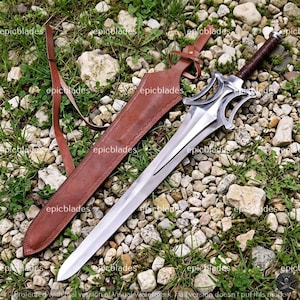 May include: A silver-colored metal sword with a double-edged blade, a complex open-work crossguard, and a dark brown leather-wrapped handle. The sword is accompanied by a matching brown leather scabbard featuring an adjustable leather strap.