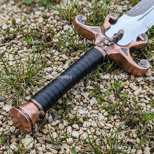 May include: A sword featuring a polished silver blade and a copper-toned metal crossguard with ornate, curved quillons. The handle is wrapped in black leather, ending in a matching copper-toned pommel. The text epicblades is visible on the image.
