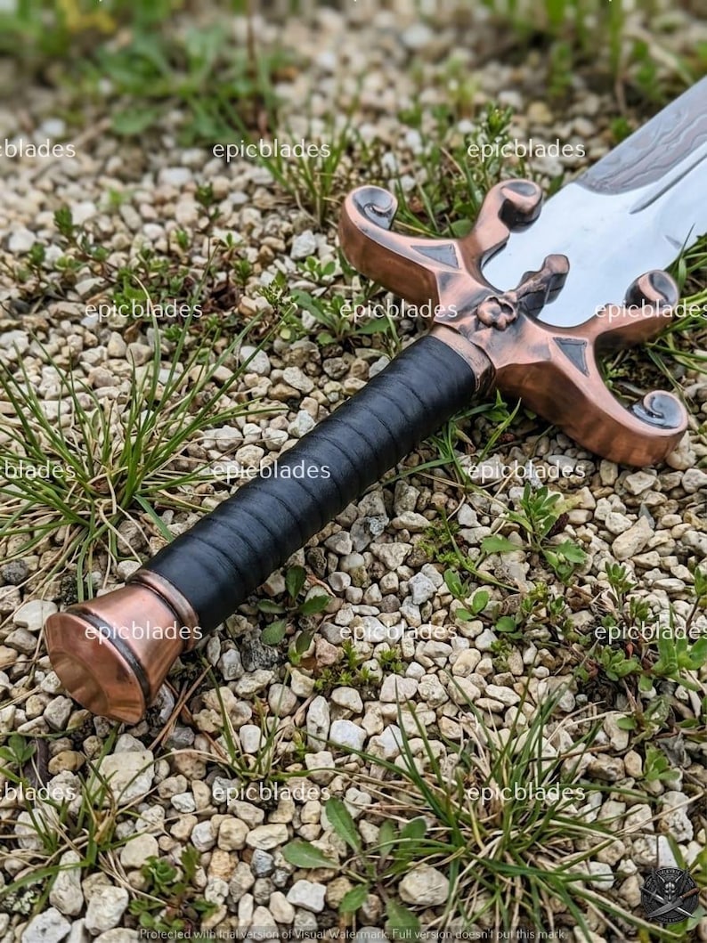 May include: A sword featuring a polished silver blade and a copper-toned metal crossguard with ornate, curved quillons. The handle is wrapped in black leather, ending in a matching copper-toned pommel. The text epicblades is visible on the image.