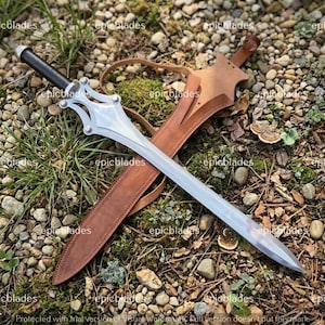 May include: A silver-colored metal sword with a black handle and a complex, multi-pointed crossguard. The sword is accompanied by a tan leather scabbard featuring a matching leather strap. The word epicblades is repeated across the image.
