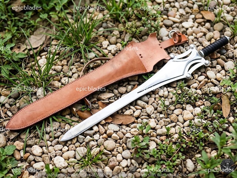 May include: A silver-colored metal sword with a black handle and a complex guard design, accompanied by a tan leather sheath featuring stitched edges and a metal ring attachment. The word epicblades is visible as a watermark across the image.