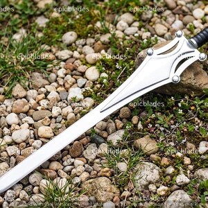 May include: A silver-colored sword with a pointed blade and a decorative guard featuring four circular accents. The handle is black with a ribbed texture and a silver pommel. The word epicblades is repeated across the image as a watermark.