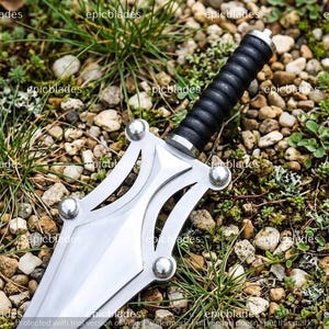 May include: A silver-colored metal dagger featuring a double-edged blade with a cut-out design and four silver rivets. The handle is black with a ribbed, cylindrical grip and a silver pommel. The word epicblades is repeated across the image.