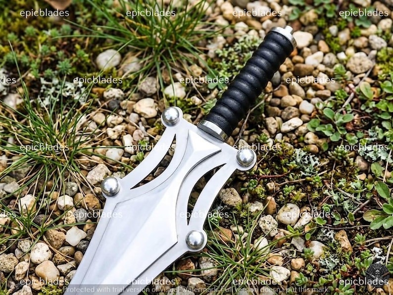 May include: A silver-colored metal dagger featuring a double-edged blade with a cut-out design and four silver rivets. The handle is black with a ribbed, cylindrical grip and a silver pommel. The word epicblades is repeated across the image.
