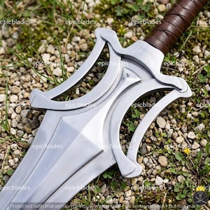 May include: A silver-colored metal sword featuring a complex, open-work crossguard with curved elements and a brown leather-wrapped handle. The blade has a central ridge and a polished finish, with the text epicblades repeated across the image.