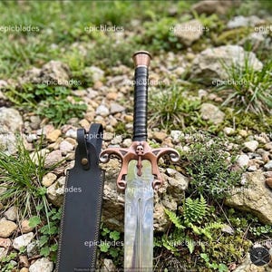 May include: A sword with a metallic blade, a black wrapped handle, and a copper-toned crossguard featuring a small skull detail at the center. The sword is accompanied by a black leather sheath with a metal snap closure and visible stitching.