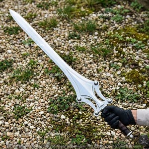 May include: A silver-colored metal sword with a pointed blade and a decorative crossguard featuring four circular rivets. The handle is wrapped in dark material, and the blade has a central ridge running down its length. The word epicblades is visible.