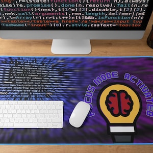 Może przedstawiać: Prostokątna podkładka pod mysz z niebieską obwódką, z fioletowo-niebieskim tłem z tekstem przypominającym kod. Posiada białą klawiaturę, mysz oraz grafikę żarówki z mózgiem i napisem "FOCUS MODE ACTIVATED".
