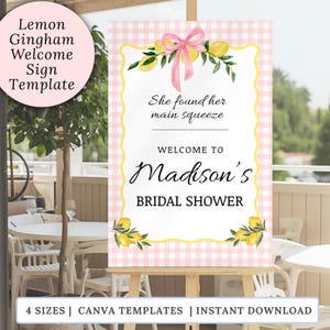 Può includere: Un cartello di benvenuto rettangolare con sfondo a quadretti vichy rosa e bianco, bordo smerlato giallo, illustrazioni di limoni ad acquerello e un nastro rosa. Il testo recita: She found her main squeeze, WELCOME TO Madison's BRIDAL SHOWER.