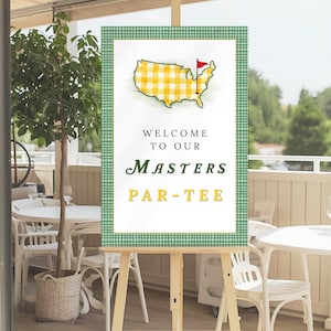 May include: A wooden easel displays a sign with a green and white checkered border. The sign features a yellow and white checkered outline of the United States with a red flag, and the words "WELCOME TO OUR MASTERS PAR-TEE."