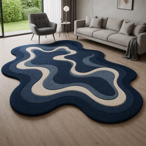 May include: An irregular, organic-shaped area rug featuring layered, wavy bands of colour. The design consists of deep navy blue, medium blue, and cream-coloured sections that create a flowing, multi-dimensional effect across the floor surface.