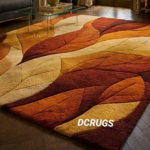 transitional, and classic interiors. The organic shapes soften structured furniture lines, and the warm color scheme enhances cozy seasonal décor themes. Ideal for homeowners seeking a statement carpet that combines artistic design, texture, and comfort, this rug transforms the room into a welcoming and elegant retreat.
The rug is styled in an elegant, upscale living room with rich dark wood herringbone flooring that enhances the warmth of the rug’s color palette. Its rectangular