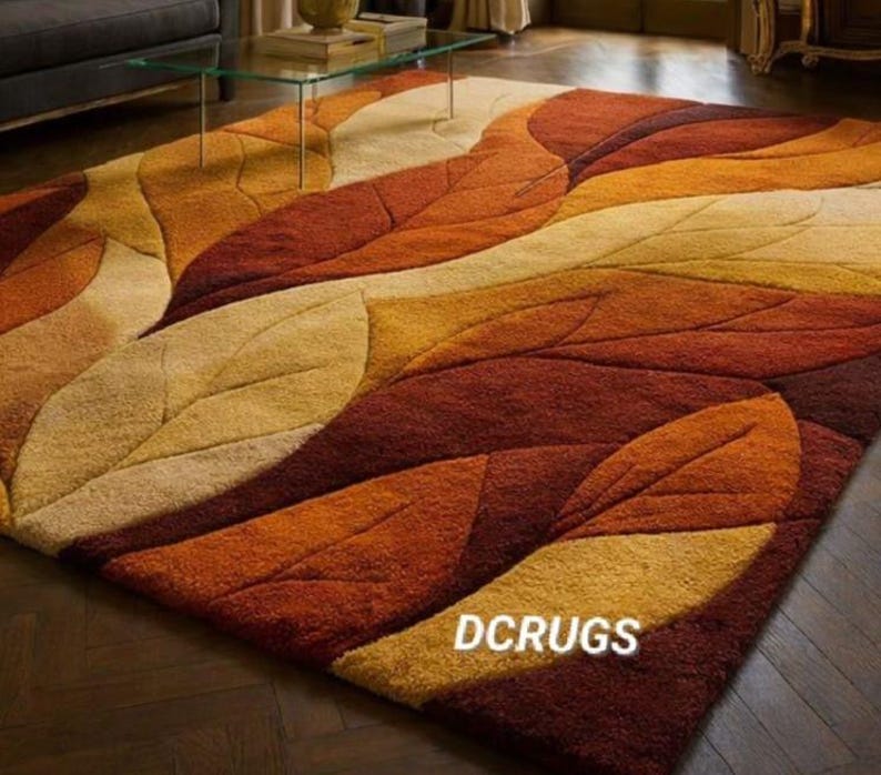 transitional, and classic interiors. The organic shapes soften structured furniture lines, and the warm color scheme enhances cozy seasonal décor themes. Ideal for homeowners seeking a statement carpet that combines artistic design, texture, and comfort, this rug transforms the room into a welcoming and elegant retreat.
The rug is styled in an elegant, upscale living room with rich dark wood herringbone flooring that enhances the warmth of the rug’s color palette. Its rectangular