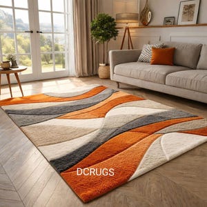 May include: A rectangular rug featuring a flowing design in orange, grey, beige, and white. The rug is laid on a wooden floor in a living room. The text "DCRUGS" is displayed on the rug.