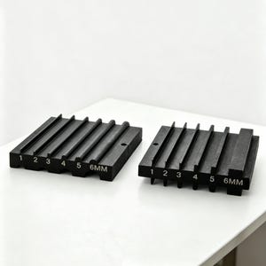 Könnte beinhalten: Zwei schwarze, rechteckige Metallblöcke mit parallelen Rillen und nummerierten Schlitzen von 1 bis 5, wobei der letzte Schlitz mit 6MM beschriftet ist. Die Blöcke haben eine matte Oberfläche und gleichmäßige Abstände zwischen den Stegen.