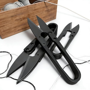 May include: A selection of black thread snips and scissors, alongside a wooden box containing spools of thread. The thread snips vary in size and design, featuring sharp blades for accurate cutting. The scissors are metal with a matte finish.