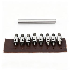 May include: A set of metal hole punch tools with a brown leather strip. The tools are silver and have a screw-like design. A silver metal rod is also included. The leather strip has several punched holes.