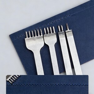 Può includere: Un set di strumenti argentati per la lavorazione della pelle, tra cui punzoni a forcella e uno strumento a singola punta, esposti su un astuccio in pelle blu navy. Gli strumenti sono disposti in fila, mostrando le loro diverse configurazioni di punte.
