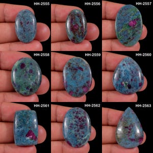 May include: A collection of nine polished kyanite and ruby cabochons in various shapes including oval, pear, and rectangular. Each gemstone displays a mottled blue and green base with distinct inclusions of deep red ruby crystals and labels HH-2555 through HH-2563.