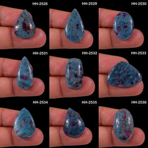 Könnte beinhalten: Eine Sammlung von neun polierten Cabochon-Edelsteinen mit einer blauen Basis und eingelagerten dunkelroten Einschlüssen. Jeder Stein ist mit den Codes HH-2528 bis HH-2536 beschriftet und zeigt verschiedene Formen wie Tropfen, Oval und Dreieck.