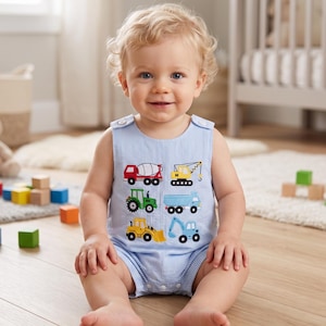 May include: A light blue and white pinstriped sleeveless romper featuring embroidered construction vehicle graphics, including a red cement mixer, yellow crane, green tractor, blue dump truck, yellow bulldozer, and a blue excavator on the front.