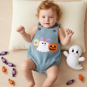 Pode incluir: Um macacão azul canelado com uma aplicação bordada de um fantasma branco com um laço roxo, uma abóbora de Halloween e um doce às riscas. A peça tem dois botões castanhos nas alças e um fecho de pressão na parte inferior.