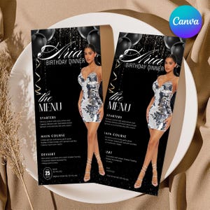 May include: Two black and silver birthday dinner menus on a white plate. The menus feature a woman in a silver sequin dress. The menu text includes "Aria Birthday Dinner" and a list of courses. Black balloons are in the background.