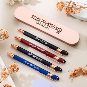 Puede incluir: Una colección de bolígrafos personalizados en varios colores, incluyendo negro, burdeos, azul marino y azul, con detalles dorados. Cada bolígrafo tiene una inscripción única, como "Paris 2026" y "Alexander". También se ve un estuche de bolígrafos en oro rosa, con el texto "STARK INDUSTRIES 20.06.1994."