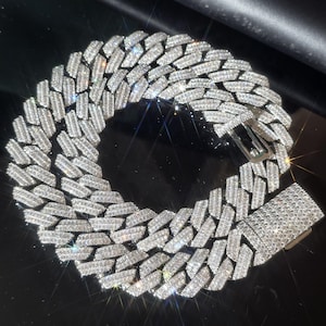 Puede incluir: Un collar de cadena de eslabones cubanos en tono plateado con un engaste denso de pequeñas piedras claras y reflectantes que cubren toda la superficie de los eslabones entrelazados y el cierre rectangular, creando un aspecto metálico brillante.