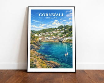 May include: A framed print featuring a coastal scene of Cornwall, England. The image showcases a vibrant blue bay with a sailboat, surrounded by rocky cliffs and a village. The sky is a bright blue with fluffy clouds. The print is displayed on a wooden floor.