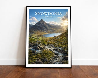 May include: Framed print of Snowdonia, Wales. The landscape features a mountain, lake, and stream under a blue sky. The text "Snowdonia Wales" is at the top of the print.